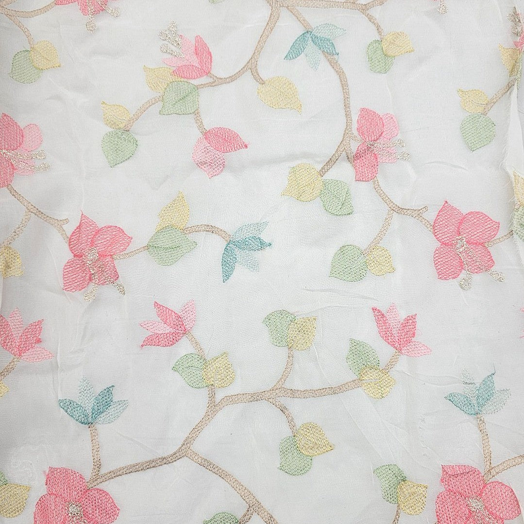 White embroidered fabric featuring a delicate floral vine pattern with pink blossoms, light green leaves, soft yellow accents, and thin tan branches.